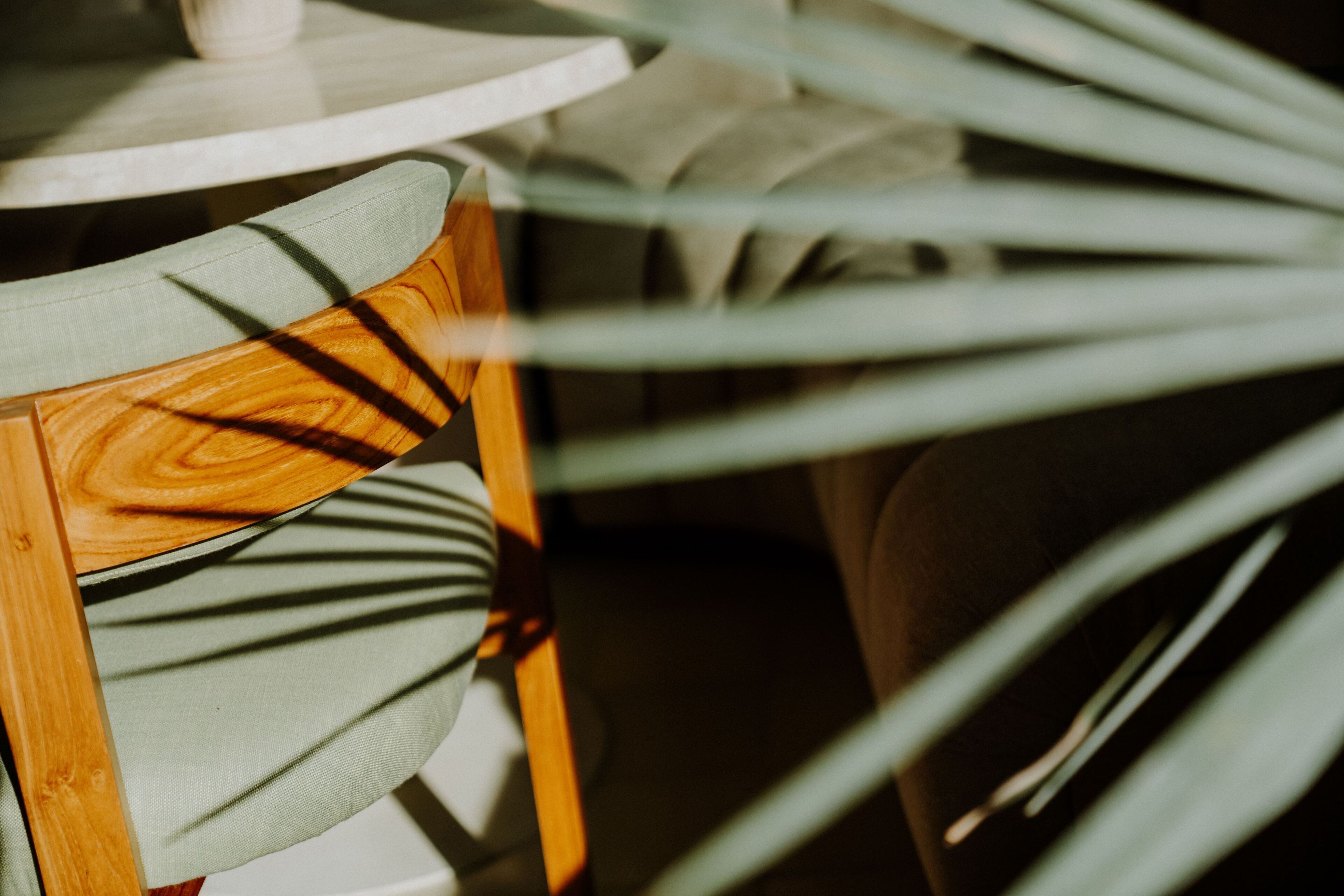 A close-up of a wooden chair with a green cushion, a white table, and a white chair with a curved backrest.