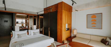 Une chambre d’hôtel moderne avec un grand lit, un canapé et une table à manger. On aperçoit un coin cuisine au fond de la pièce.