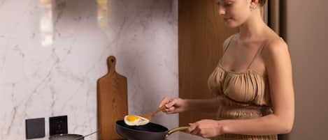 A modern kitchen with a woman cooking an egg in a pan.