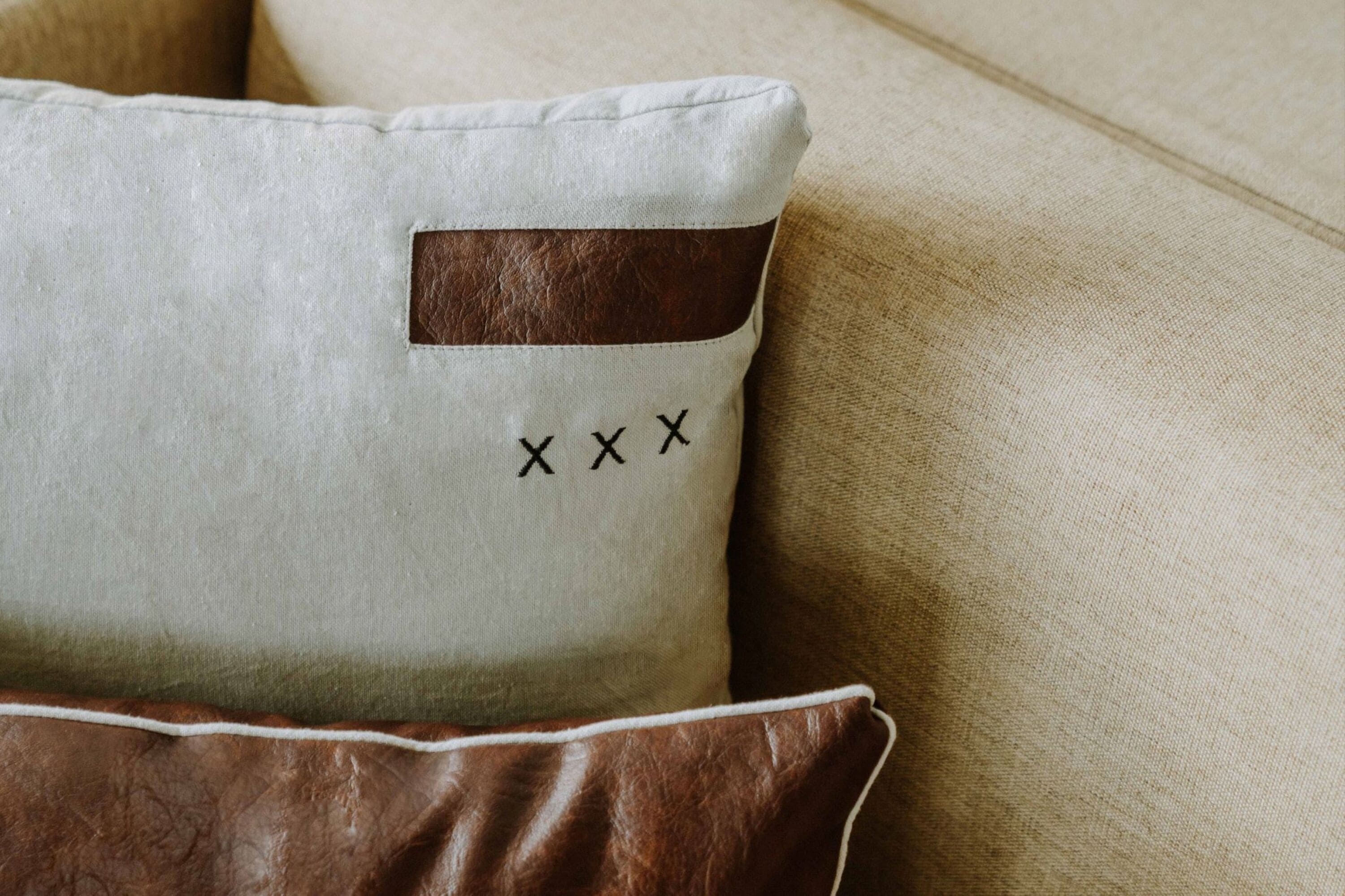 A pillow with a brown leather patch and the letters "XXX" on a beige fabric.