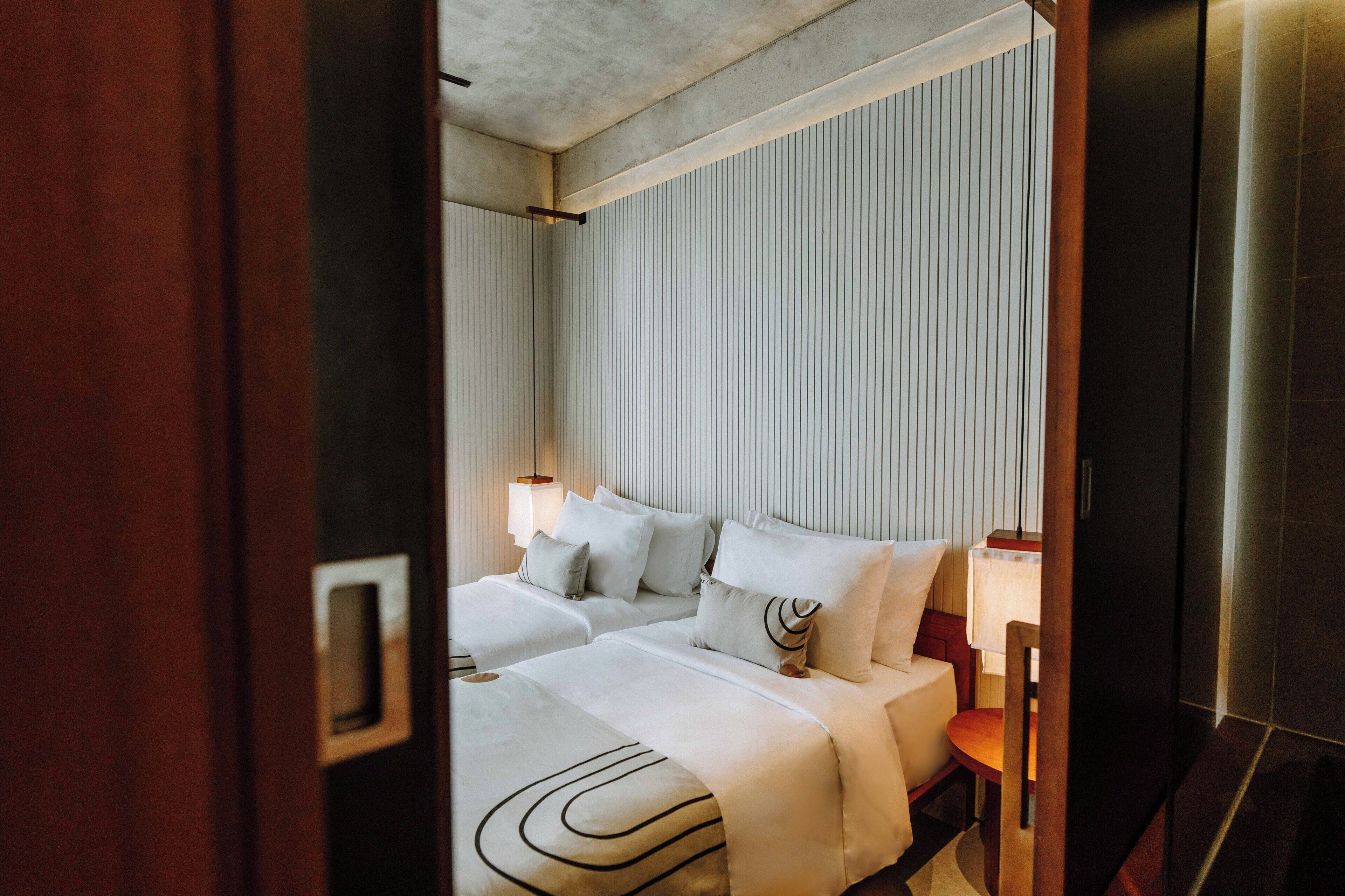 Quarto de hotel com duas camas, uma porta de madeira e uma parede com linhas verticais.