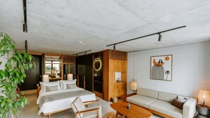 Quarto de hotel moderno com cama, sofá, cadeiras, mesa de centro e planta em vaso.