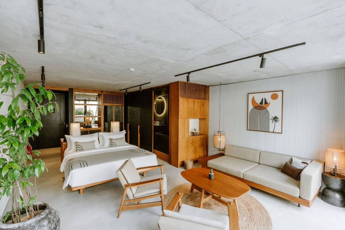 Una habitación de hotel moderna con cama, sofá, sillas, una mesa de centro y una planta en maceta.