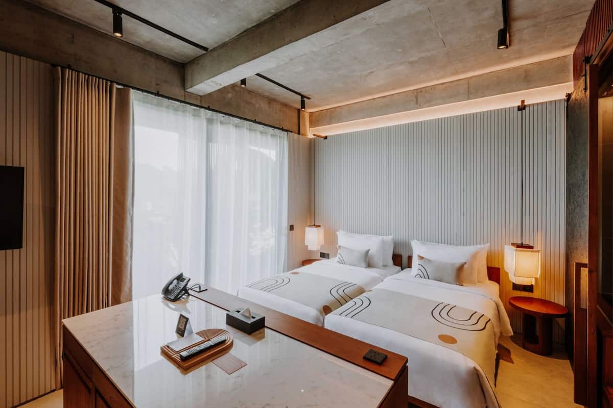 Una habitación de hotel con dos camas, un escritorio con teléfono y una mesita de noche con lámpara.