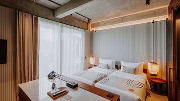 Una habitación de hotel con dos camas, un escritorio con teléfono y una mesita de noche con lámpara.