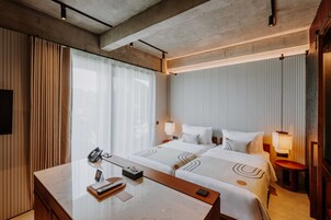 Una habitación de hotel con dos camas, un escritorio con teléfono y una mesita de noche con lámpara.