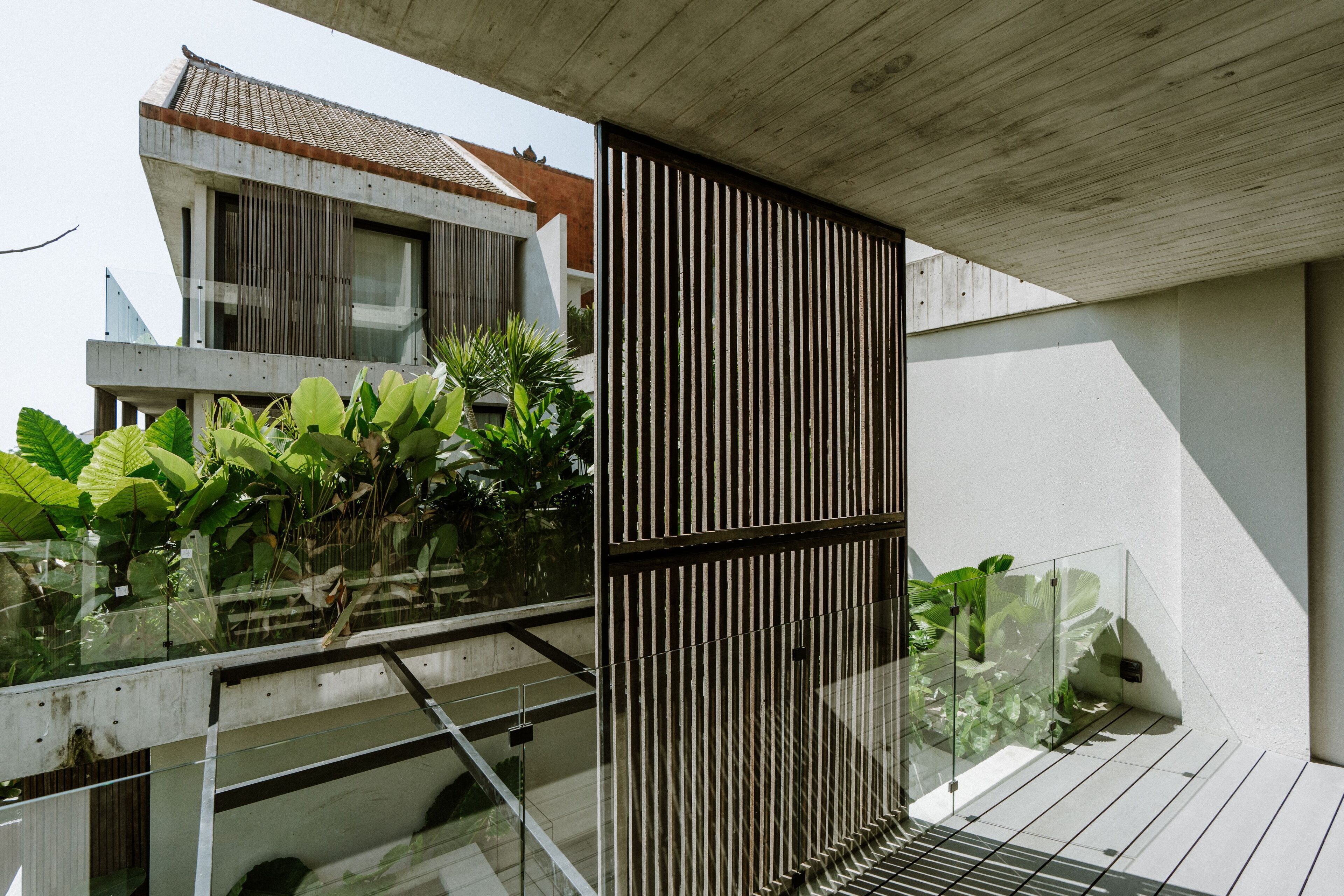A modern building with a concrete facade, large windows, and a balcony with plants.