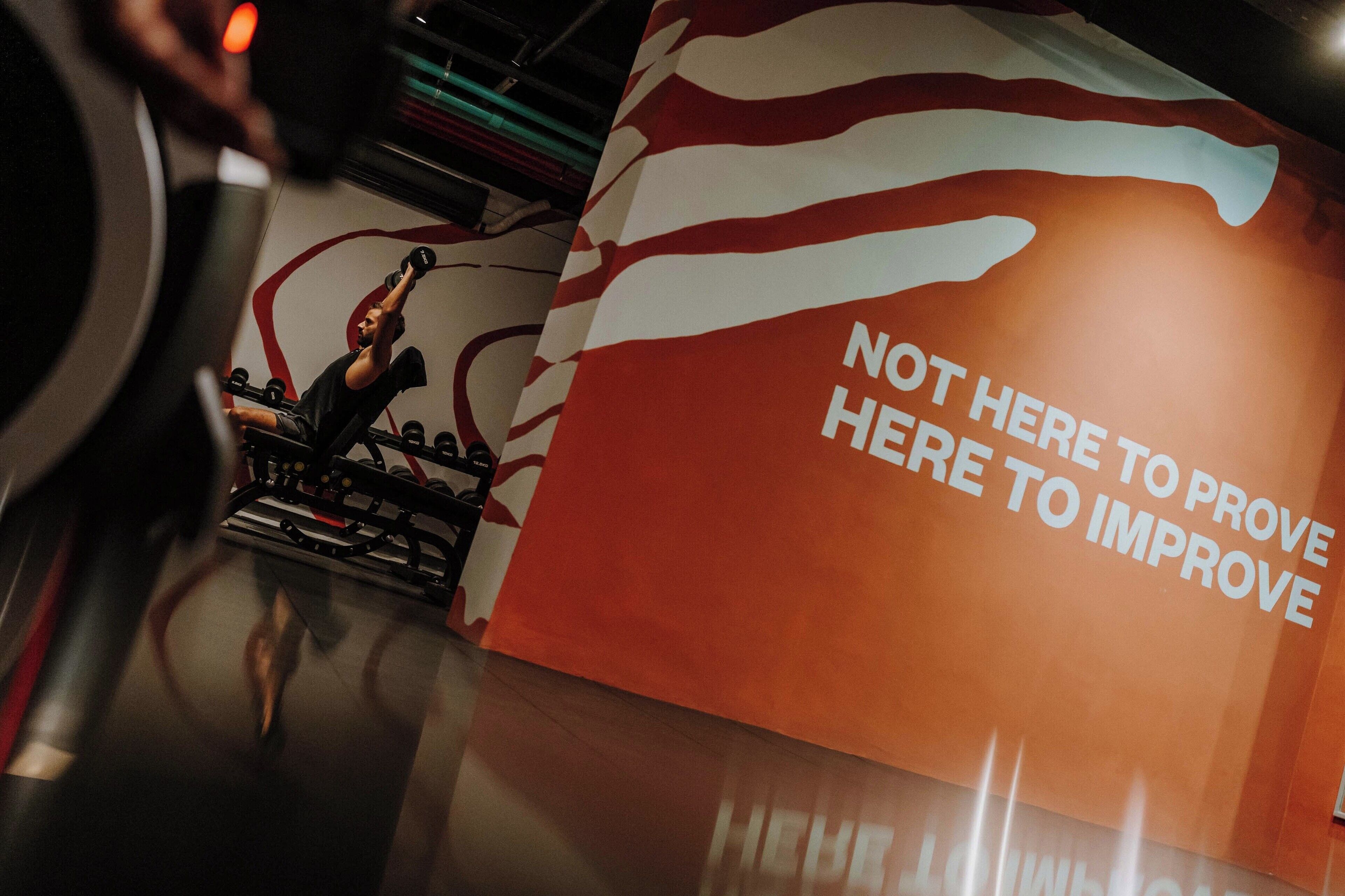 A gym with a motivational sign that reads "NOT HERE TO PROVE HERE TO IMPROVE".