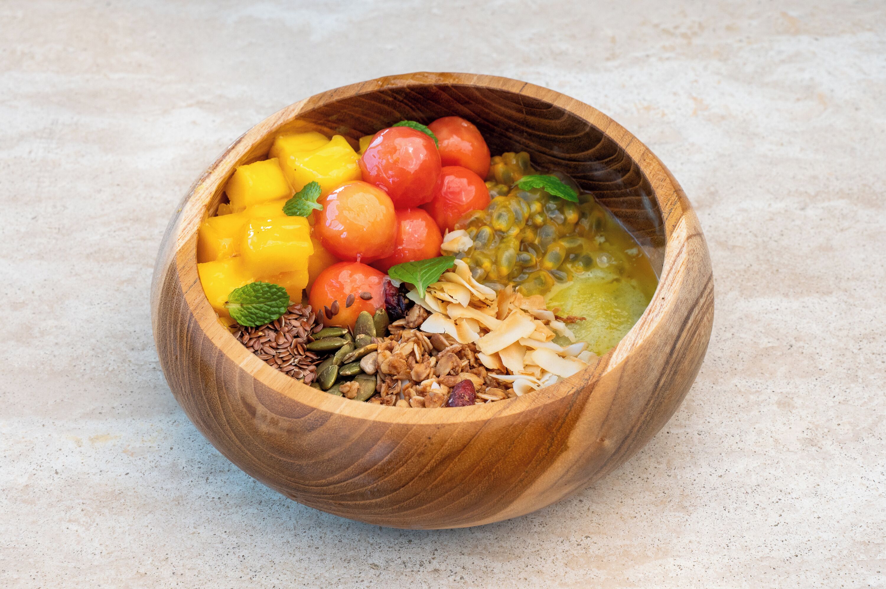 A wooden bowl filled with various fruits and nuts.