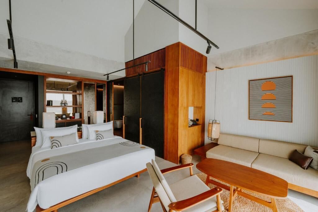 Habitación de hotel moderna con una cama grande, un sofá, una mesa de madera y vistas al área de la cocina.