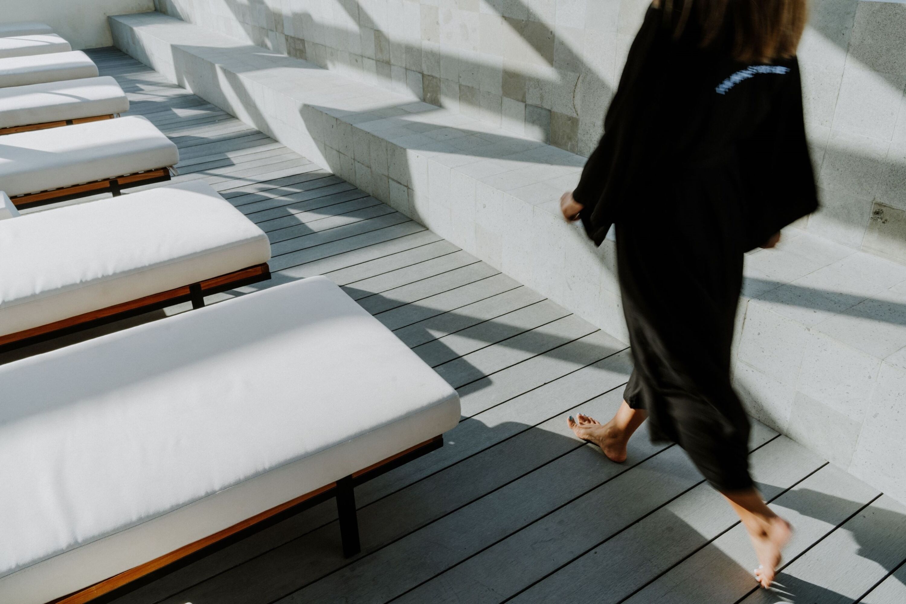 A person walking past sun loungers on a wooden deck with stone steps.