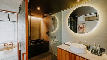 Un baño moderno con ducha envuelta en vidrio, bañera independiente, espejo redondo y tocador de madera.