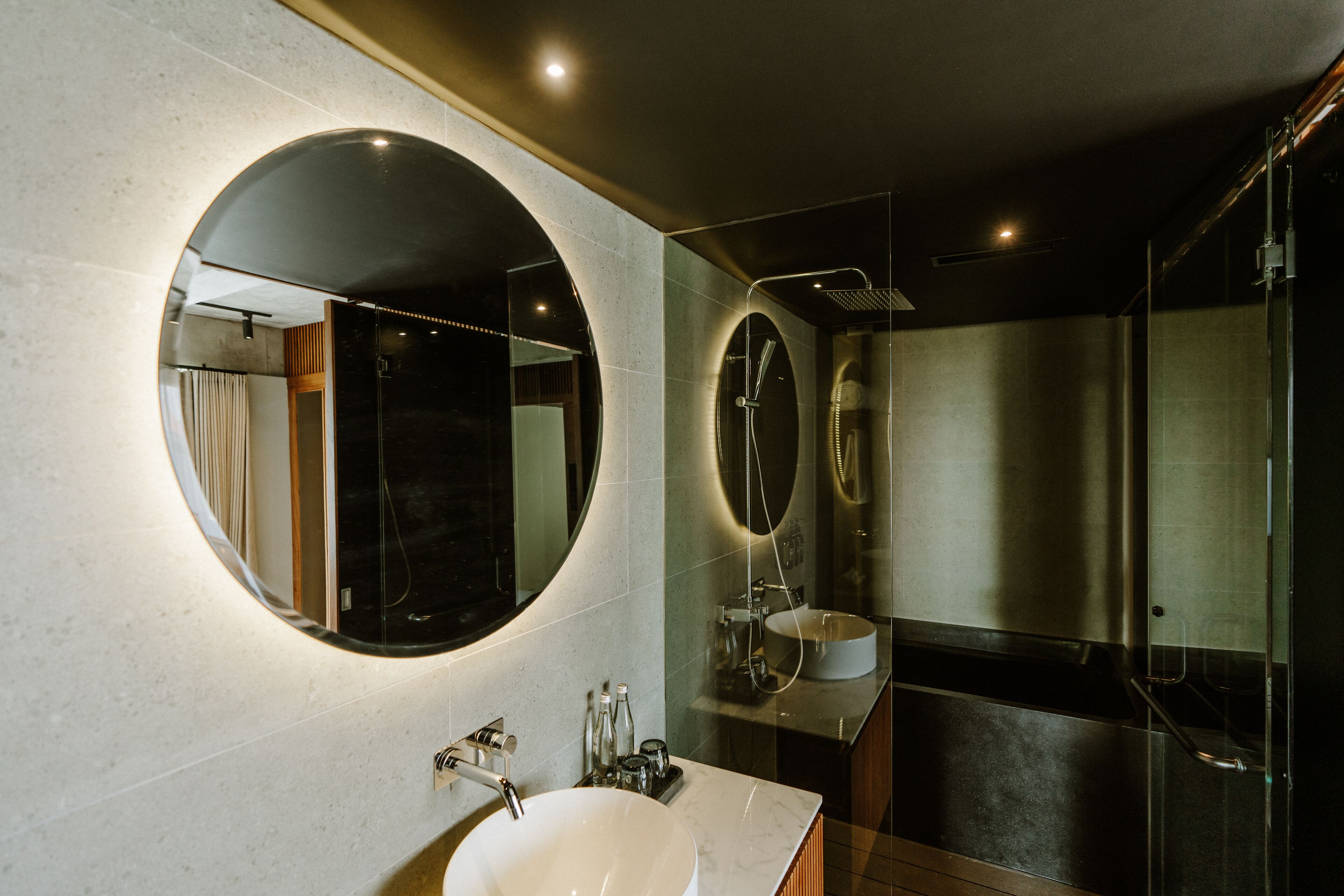 Une salle de bain moderne avec un grand miroir rond, un lavabo blanc et une douche à parois de verre.