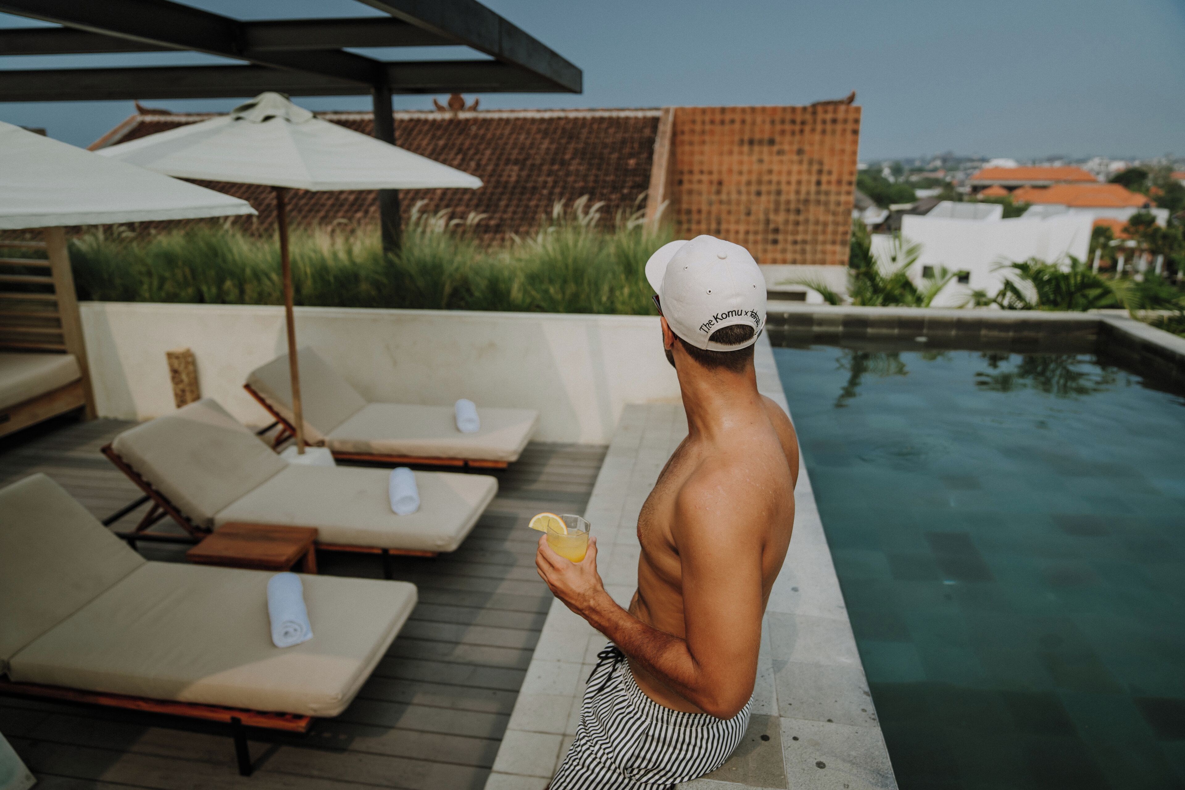 A man by a pool with lounge chairs and umbrellas.