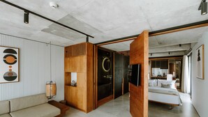 Una habitación de hotel moderna con sofá, detalles de madera, cama y baño visible a través de una puerta de cristal.