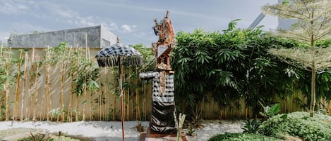 A statue in a garden with bamboo, a checkered umbrella, and a building in the background.
