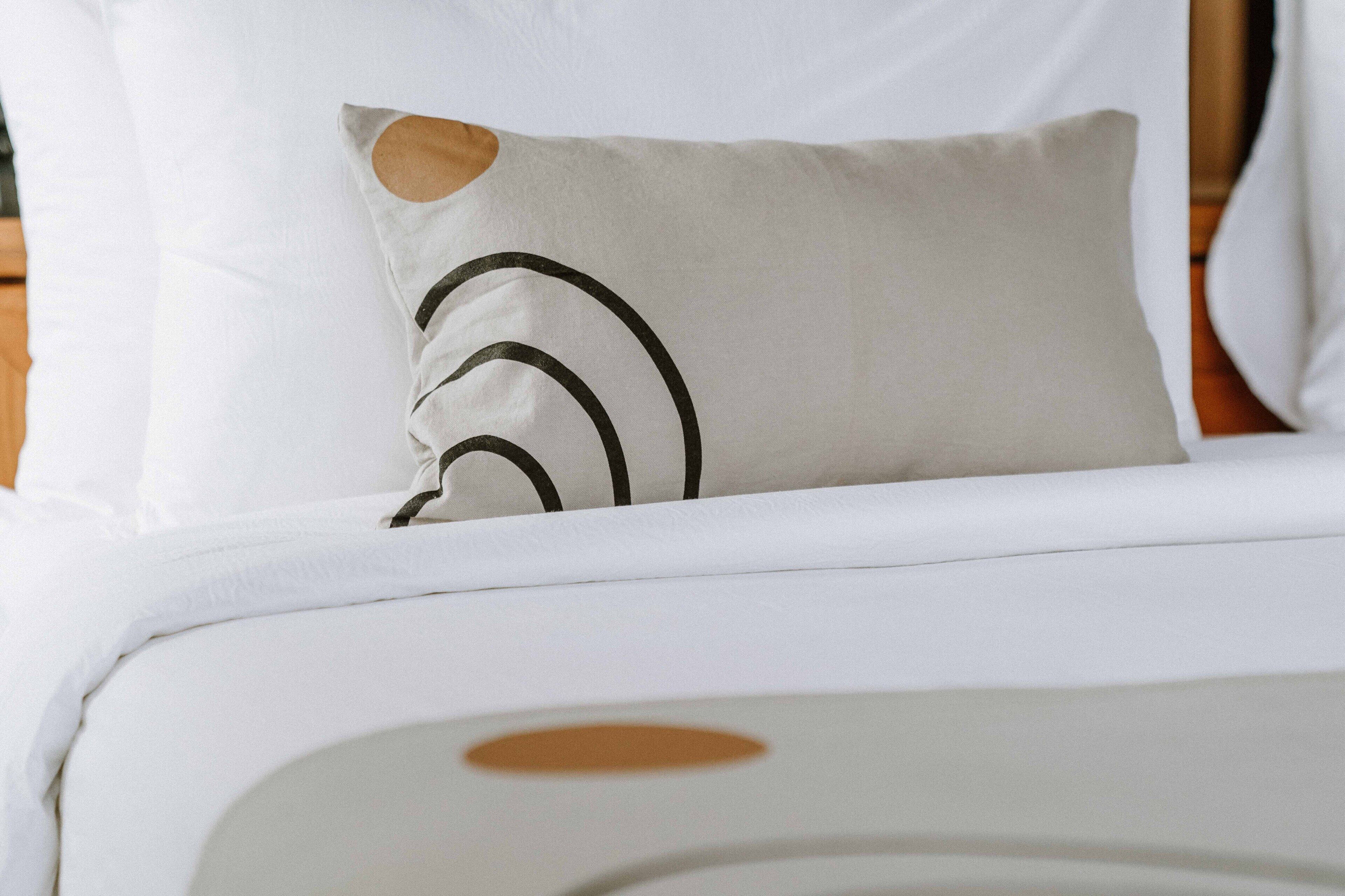 Una cama con ropa de cama blanca y un almohadón con diseño circular.