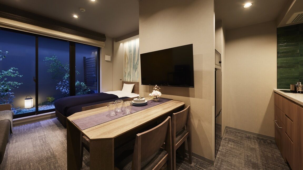Habitación de hotel con cama, escritorio con silla, televisor de pantalla plana en la pared y vistas a árboles por la ventana.