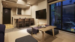 Una habitación de hotel moderna con zona de comedor, televisor en la pared y un amplio ventanal con vistas al exterior.