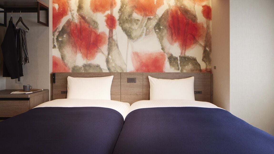 Una cama doble con ropa de cama blanca y azul, un cabecero de madera y una pared con arte abstracto.