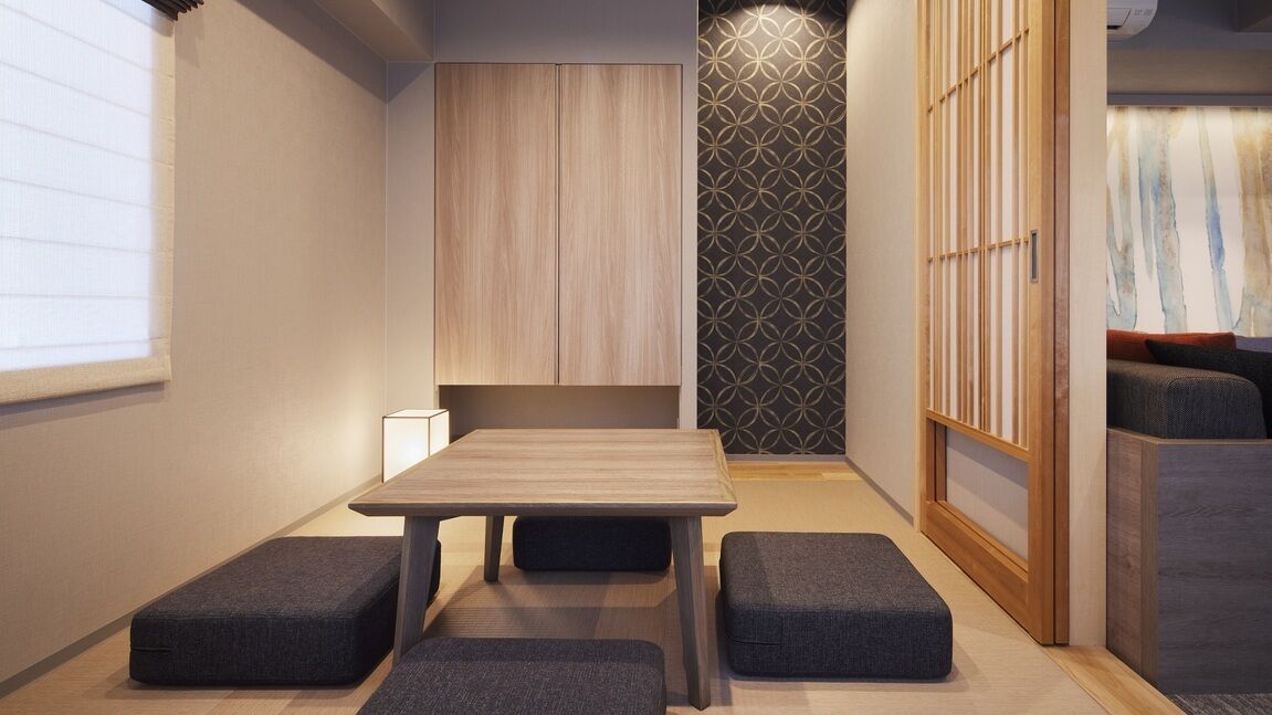 A compact room with a wooden table and four grey ottomans, a sliding door with a geometric pattern, and a wall-mounted cabinet.