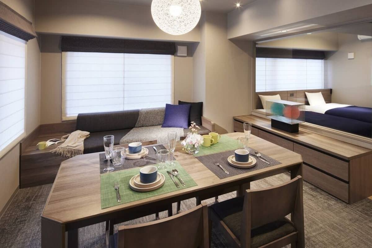 A modern hotel room with a dining area, a sofa, and a bed.