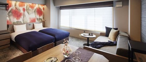 Habitación de hotel con dos camas, un sofá, una mesa de comedor con un jarrón de flores y un ventanal con persianas.
