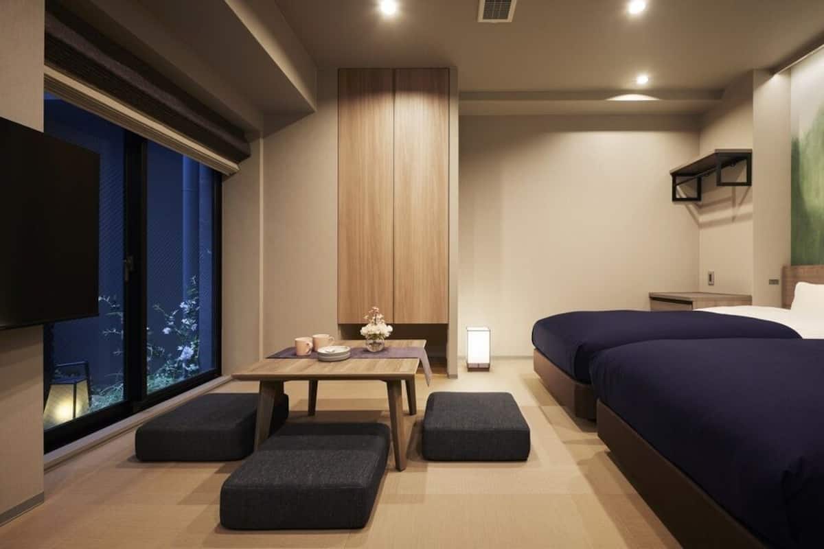 A modern hotel room with a large bed, a desk, and a view of the night sky through a window.