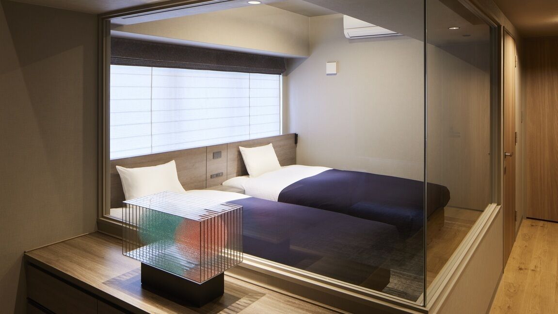 A compact hotel room with a bed, bedside tables, and a window with blinds.
