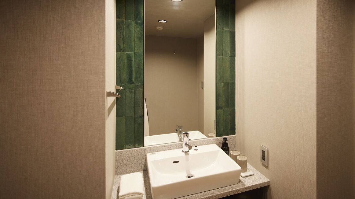 A bathroom with a white sink, a mirror, and green-tiled walls.