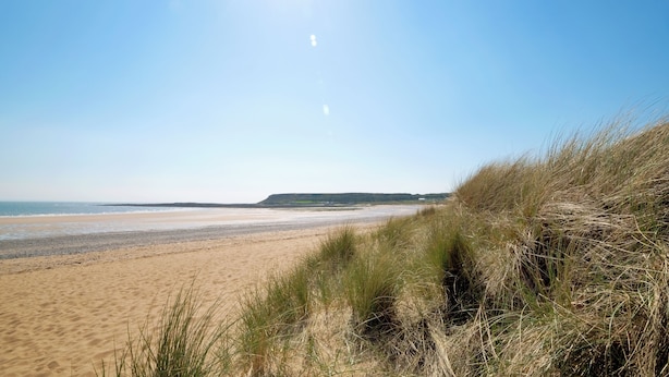 A beach with sand and grass in the foreground, a clear sky, and a distant shoreline. - The Retreat - 5 Bedroom House - Horton (Swansea)
