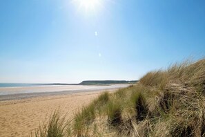 A beach with sand and grass in the foreground, a clear sky, and a distant shoreline. - The Retreat - 5 Bedroom House - Horton (Swansea)