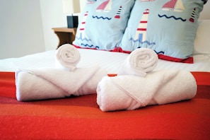 Una cama con dos toallas enrolladas sobre una manta roja.