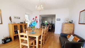 A dining area with a wooden table and chairs, a vase with flowers, and a black leather couch. - The Retreat - 5 Bedroom House - Horton (Swansea)