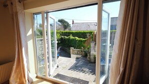 A sliding glass door leading to a patio with a stone floor, a wooden fence, and a hedge. - The Retreat - 5 Bedroom House - Horton (Swansea)