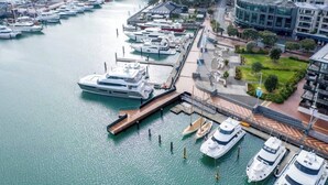 A marina with multiple yachts docked, a modern building, and a landscaped area with trees. - Princess Wharf w/ Balcony

 (Auckland)