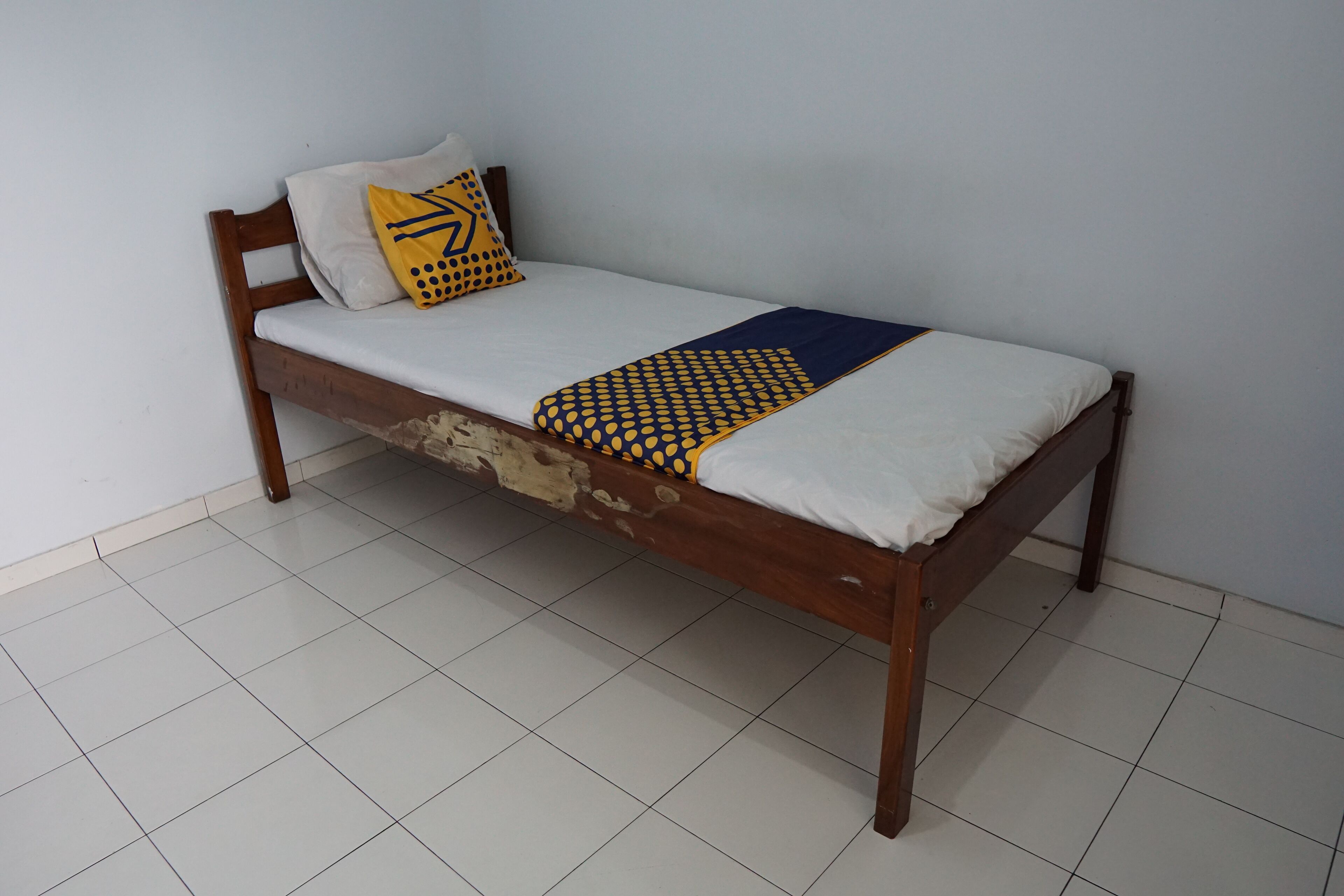 Una cama individual con estructura de madera, ropa de cama blanca y una colcha estampada.