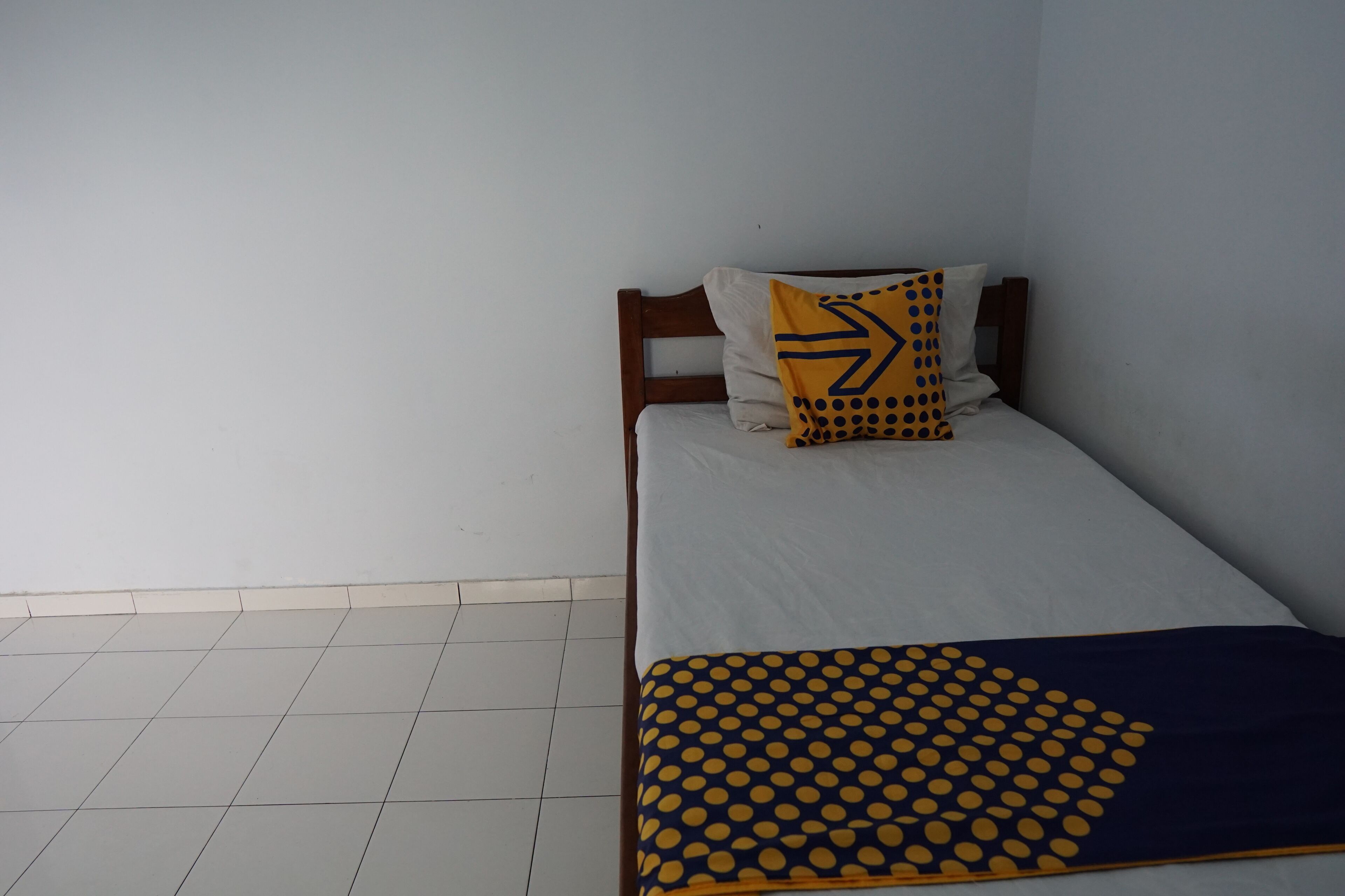 Un lit simple avec une tête de lit en bois, un matelas blanc et une couverture à pois bleus et jaunes.