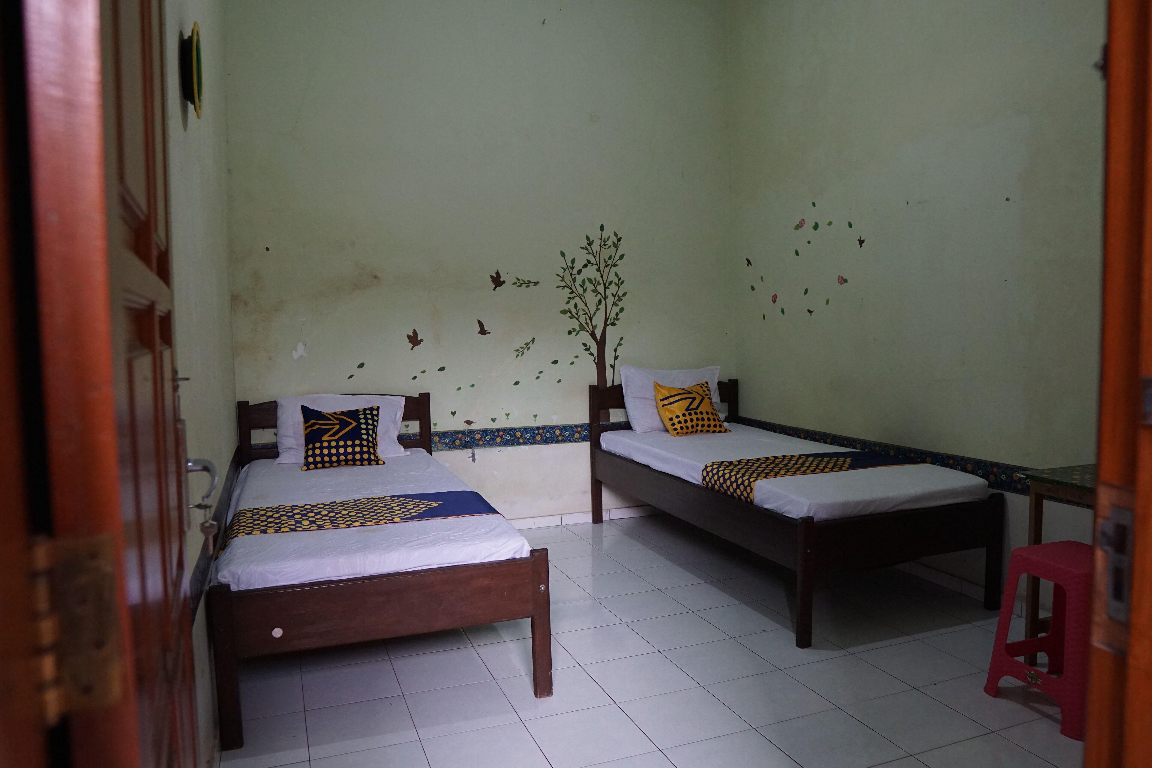 A room with two wooden beds, white bedding, and a red stool.