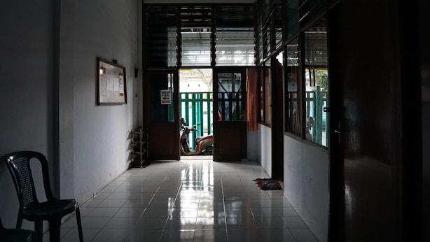 A hallway with a scooter parked at the end, a chair, and a door leading outside. - Hotel O Yoko Kost Syariah (Bondowoso)