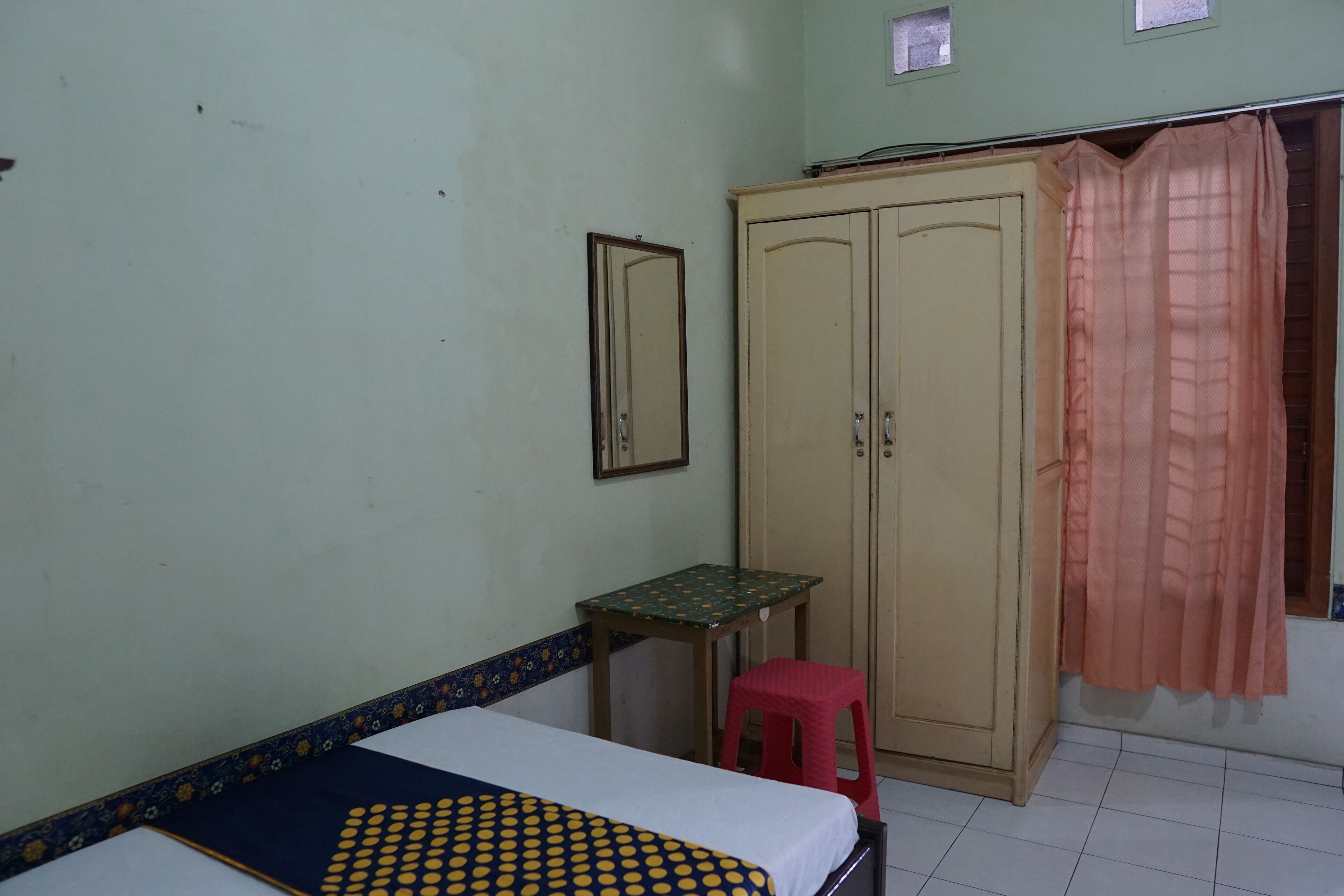Un dormitorio con cama, armario, una mesita y un taburete.