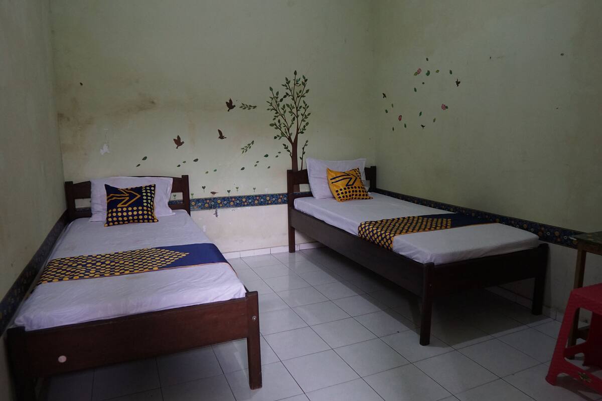 Two single beds with wooden frames and white bedding, a small red stool, and a wall with a tree decal and bird decals.