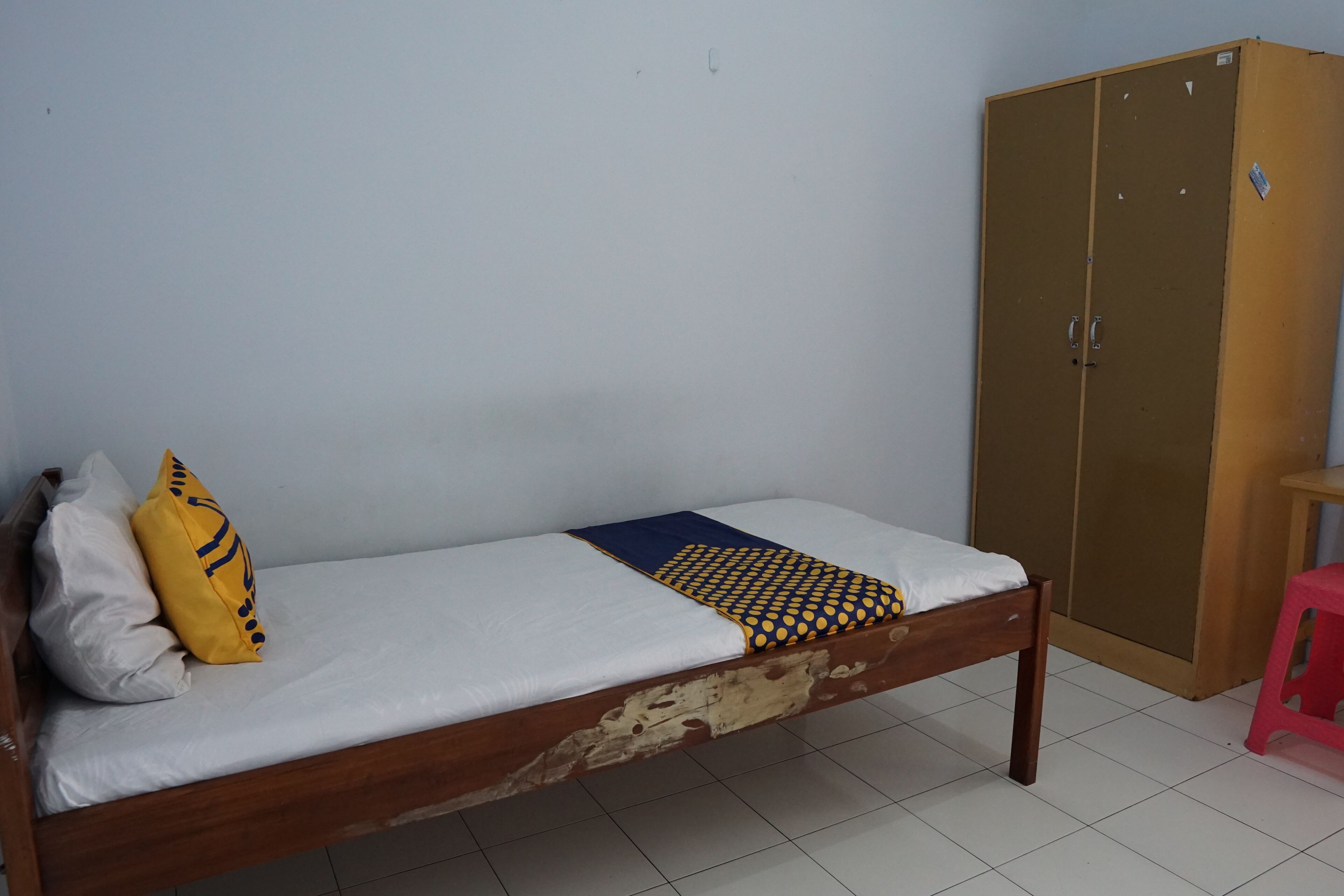 A single bed with a wooden frame, a white mattress, and two pillows. There is a wardrobe with a brown door to the right of the bed.
