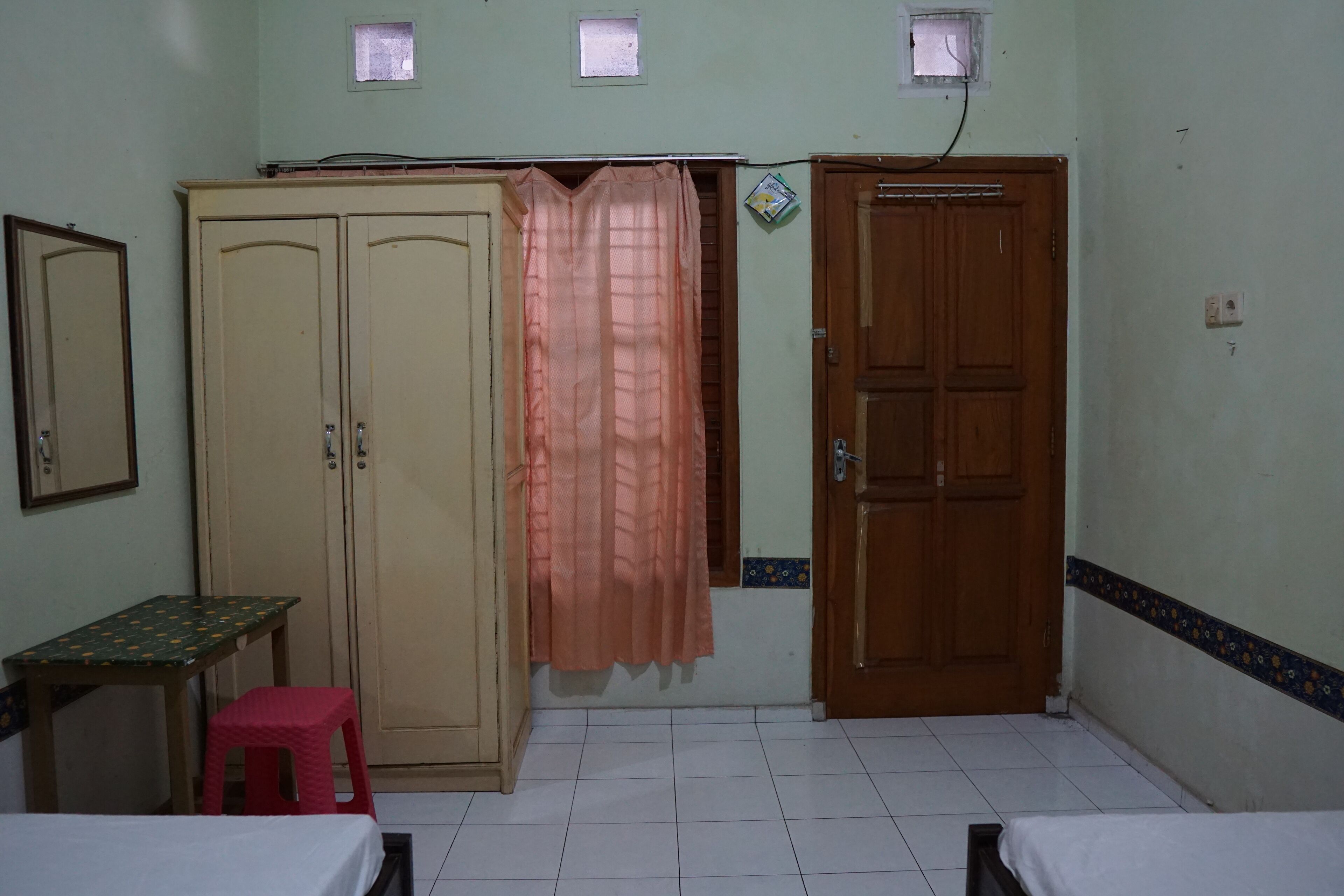 Una habitación con dos camas, un armario, una mesita y un taburete rosa.