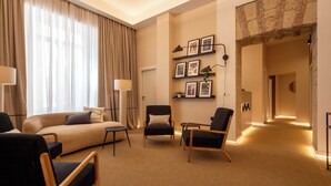 A hotel room with a sofa, two armchairs, a small table, and a lamp. There are framed pictures on the wall and a carpeted floor. - Mamalu Studios and Suites (Naples)
