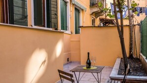 A small outdoor patio with a table and chairs, a bottle of wine, and a tree. - Porpora Home@ Venice (Venice)