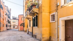 A narrow street with buildings on either side, featuring balconies with plants, a visible door with a number, and a clear sky. - Porpora Home@ Venice (Venice)
