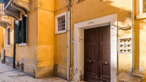 A narrow street with a yellow building featuring a large wooden door and a small window. - Porpora Home@ Venice (Venice)