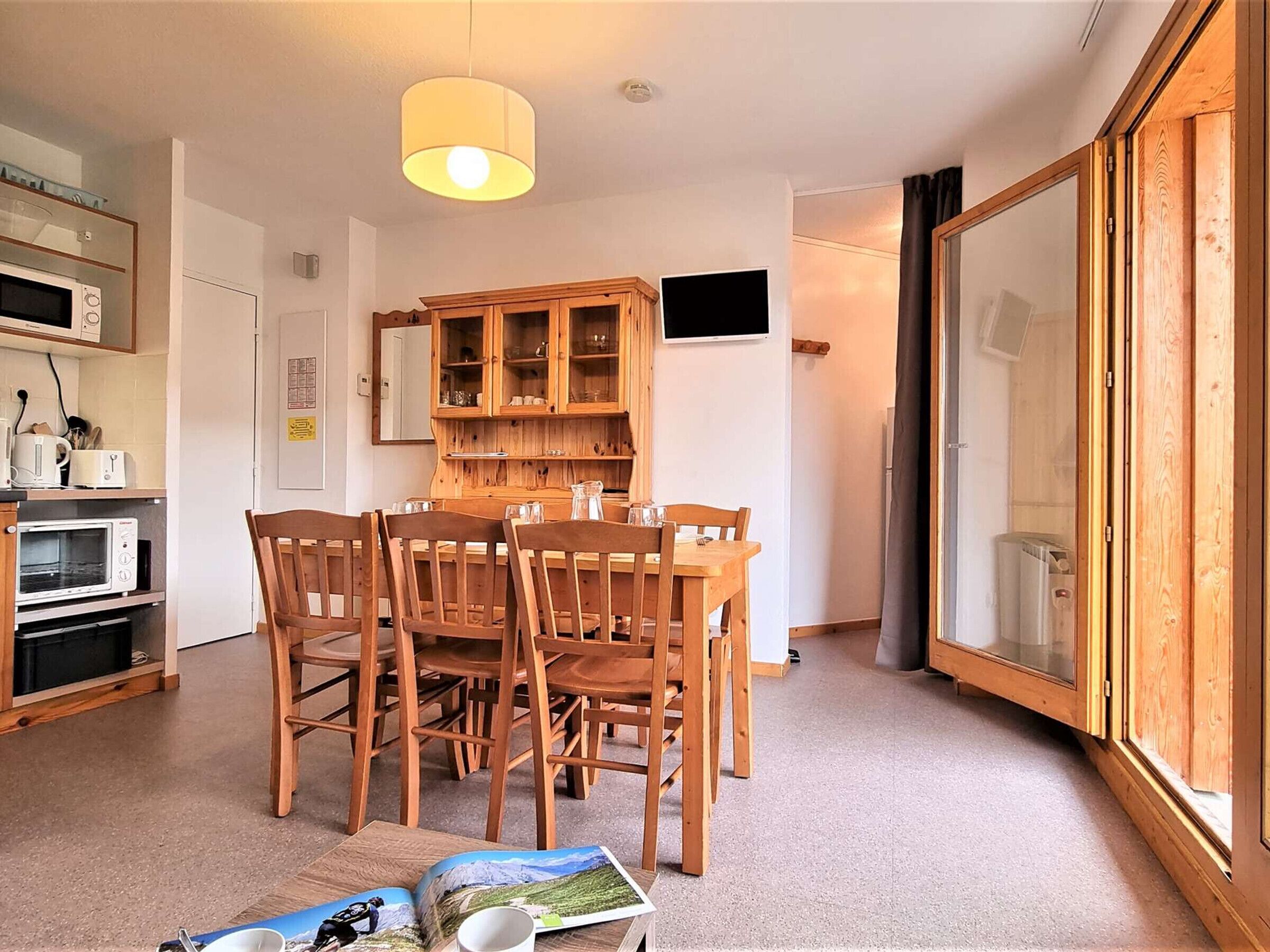 Un espace de vie compact comprenant un coin repas, des meubles de rangement en bois, un téléviseur et une grande porte-fenêtre coulissante.