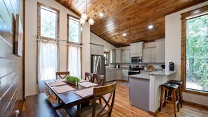 Een houten interieur met een eethoek, keuken en grote ramen.